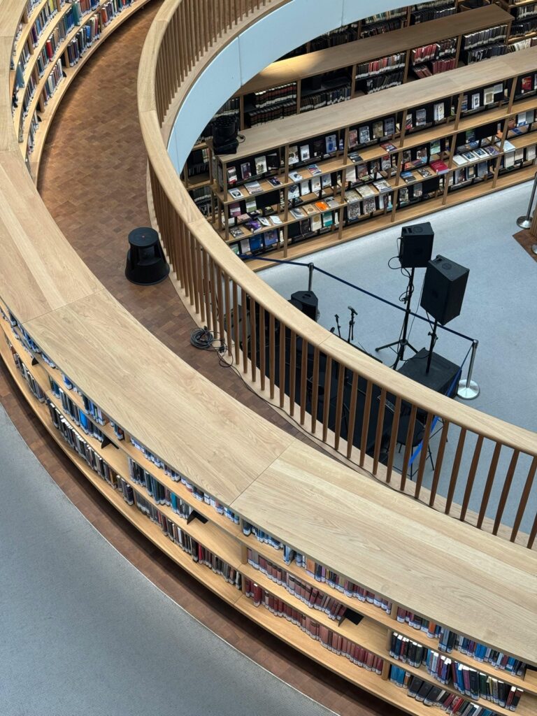 Curved library shelves with books and a stage setup for events in a modern interior.
